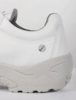 Preview: The image displays the side of a white athletic shoe with a gray sole. The shoe has a smooth surface, featuring a small round marking. The interior is slightly gray and cushioned.