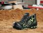 Preview: The image shows a black work shoe with green accents. It features a sturdy sole, laces, and a sporty design. The background is sand-colored and blurry.