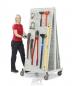 Preview: A woman with blonde hair in a red shirt stands next to a mobile tool stand. The stand contains various tools such as pliers, hammers, and a level, all neatly hung up.