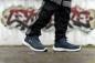 Preview: In the image, there are simple, sporty shoes in dark blue with white soles. The person is wearing black, loose pants. In the background, there is a graffiti-like, colorful wall print.