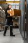 Preview: A man is carrying a large box in a warehouse. He is wearing black work clothes and is standing between shelves. The room has a high ceiling and is well-lit.