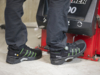 Preview: The image shows feet in black work shoes with green accents. A person is standing next to a machine unit in an industrial setting. The floor is bright and smooth.