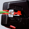 Preview: The image shows a wire cutter gripping a green and a brown wire. The cutter has a black and red color scheme and displays the cutting surfaces for the wire.