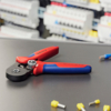 Preview: The image shows a crimping tool with red and blue handles on a dark table. In the background, colored terminal connectors and cables are visible.