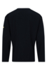 Preview: The image shows a black, long-sleeved top made of a textured fabric. It features a simple cut with a round neckline and a small, yellow detail on one sleeve.