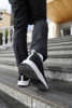 Preview: A person is walking up the stairs, wearing black sports shoes with white details and black pants. In the background, yellow and gray wall surfaces are visible.