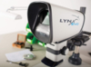 Preview: The image shows a device called LYNX Evo, which looks like a small telescope. It has a black opening at the front, a gray and white casing, and is mounted on a stable gray base.