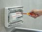 Preview: A craftsman is working on an electrical distribution box on a wall. He is holding a red screwdriver and is screwing on components in the box, which appears illuminated and modern.