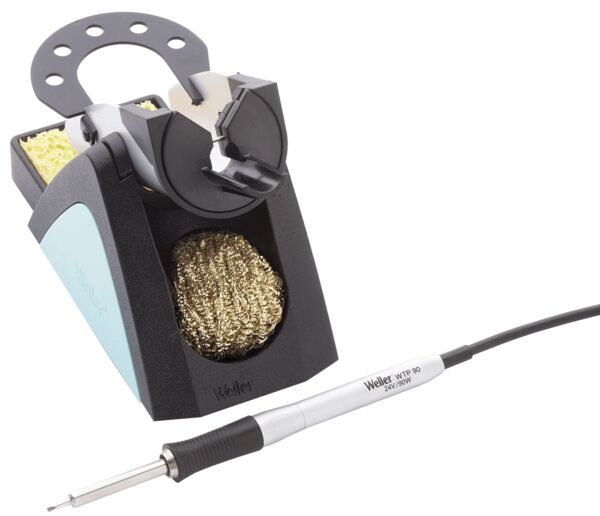 The image displays a soldering station. At the top, there is a holder for a soldering iron, below which are a sponge and golden metal wool for cleaning. A silver soldering iron is connected.