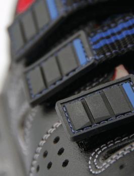 The image shows a part of a black shoe with several straps. The straps are made of a sturdy material and have black Velcro fasteners that are slightly protruding.