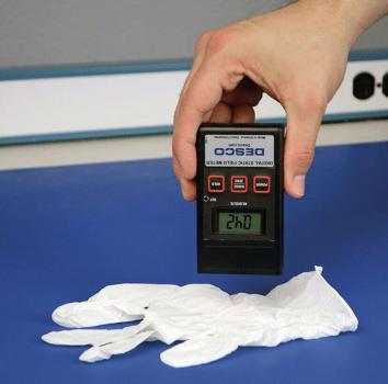 A hand holds a measuring device over white disposable gloves. The digital display shows a number, while the background is blue.