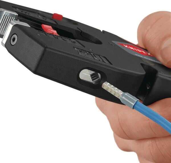 The image shows a hand holding a black tool used for stripping wires. A blue wire is inserted into the tool and is currently being processed.