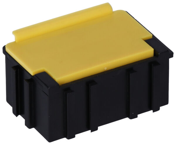 The image shows a small, rectangular container. It has a black bottom and a yellow lid, which is slightly curved. The sides are vertical and smooth, with some grooves.