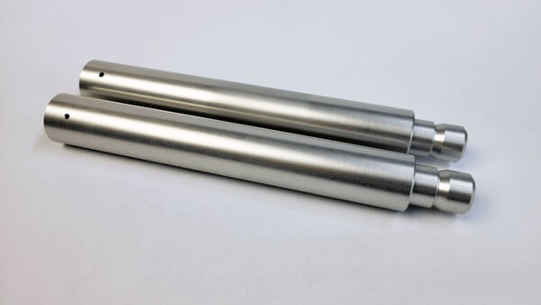 The image shows two elongated, silver metal cylinders lying parallel to each other. They have a smooth surface and a larger diameter at one end.