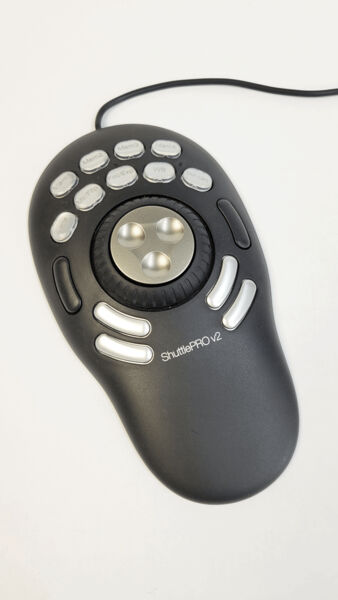 The image shows an oval, black controller with a central round dial and several buttons. The controller has a wired connection and is intended for multimedia applications.