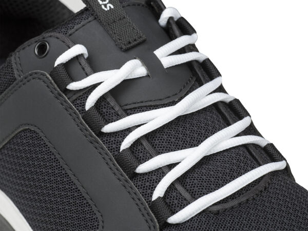 The image shows a black sports shoe with white, braided laces. The surface texture appears breathable, featuring a simple, modern design.