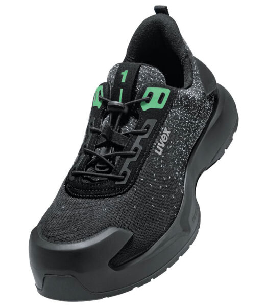 The shoe is a sporty sneaker with a black surface that has small, bright dots. It features green accents and a sturdy, rubberized sole edge for good grip.