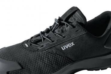 Das Bild zeigt einen schwarzen Sportschuh mit einem modernen, schlichten Design. Die Oberfläche besteht aus einem atmungsaktiven Material, und die Schnürsenkel sind gut sichtbar. Das Logo "uvex" ist sichtbar.