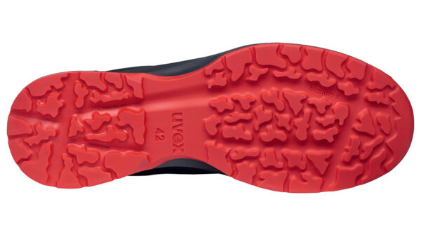 The image shows the underside of a shoe. The sole is black with a red tread. The pattern consists of irregular indentations and cleats that provide good traction.