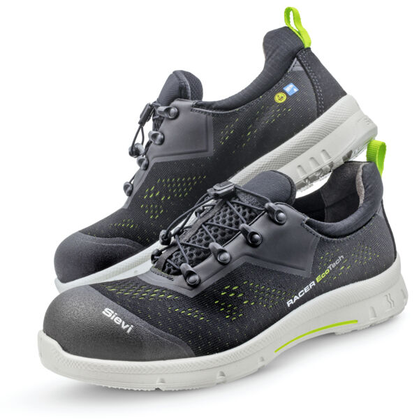 The image shows a pair of black safety sneakers with light green accents. They feature a padded, non-slip sole and pointed reinforcements for foot protection. Laces are included.