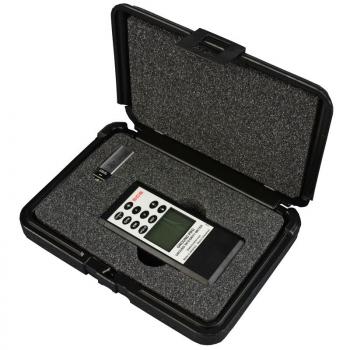 The image displays an electronic measuring device in a black, sturdy storage box. The device features a screen and buttons for various functions, all set within a foam-padded interior.