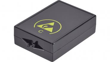 The image shows a black, rectangular box with a circular, yellow logo depiction on the top. On the front, there is a small lever or button.