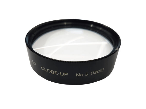 The image shows a round macro filter made of black metal with a smooth, transparent glass surface. On the filter, it reads "CLOSE-UP No.5" and a serial number. The filter is used for close-up photography.