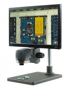 The image shows a screen displaying an enlarged view of a circuit board. Next to it is a camera for magnification, mounted on a sturdy tripod.