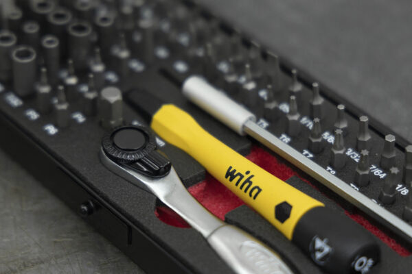 The image shows a toolbox with various screwdrivers and a ratchet tool. Some bits are arranged in a black-red holder. A yellow handle is clearly visible.