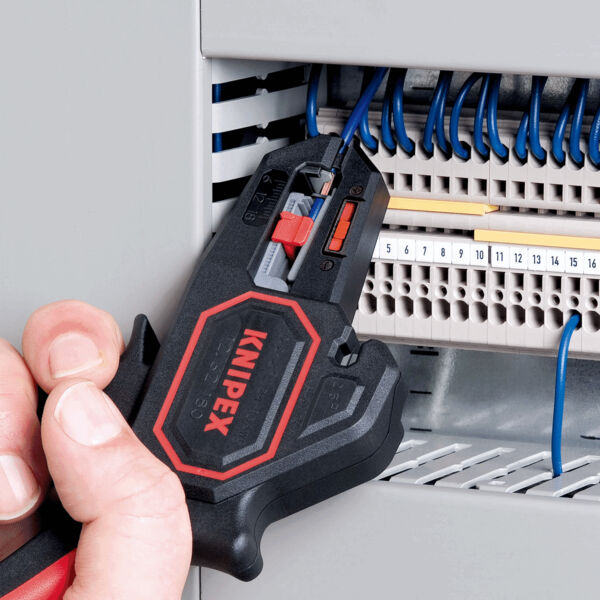 The image shows a hand holding a black tool with a red handle. It is being inserted into a gray switch cabinet, where several blue wires are visible.