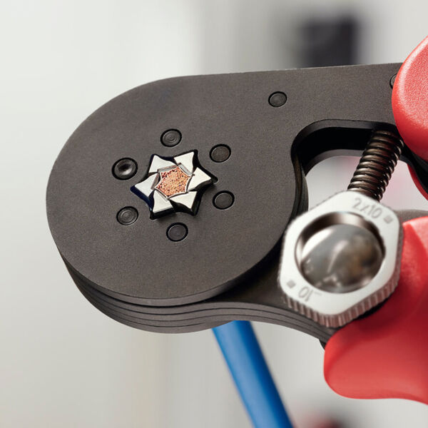 The image shows a tool with a black, round main surface. In the center, there is a star-shaped relief. Red handles are visible, and an adjustment screw is present.