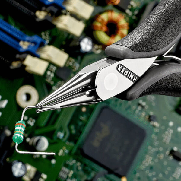 The image shows a pair of tweezers holding a small electronic resistor. The resistor has colored stripes and stands out against a green circuit board in the background.