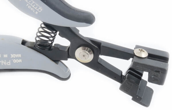 The image shows a pair of pliers with gray and black handles. It features a spring mechanism and a special device at the tip that is used for gripping or cutting.