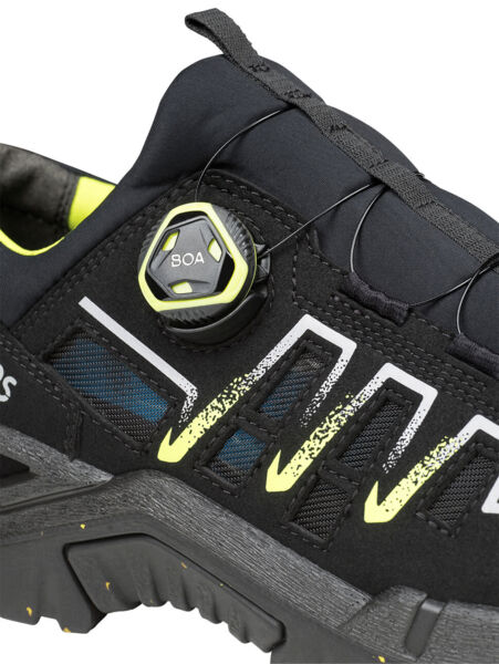 The image shows a black sports or hiking shoe with yellow and gray accents. It features a quick-lacing system using a twist knob, which facilitates adjustment.