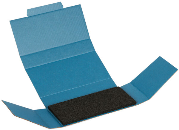 The image shows an open blue box. In the center lies a black, rectangular piece of foam. The box has two side flaps and a lid.