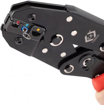 The image shows a black crimping tool with a red handle. The tool has a mechanism for connecting cables and an opening with colored markings (blue, red, yellow).