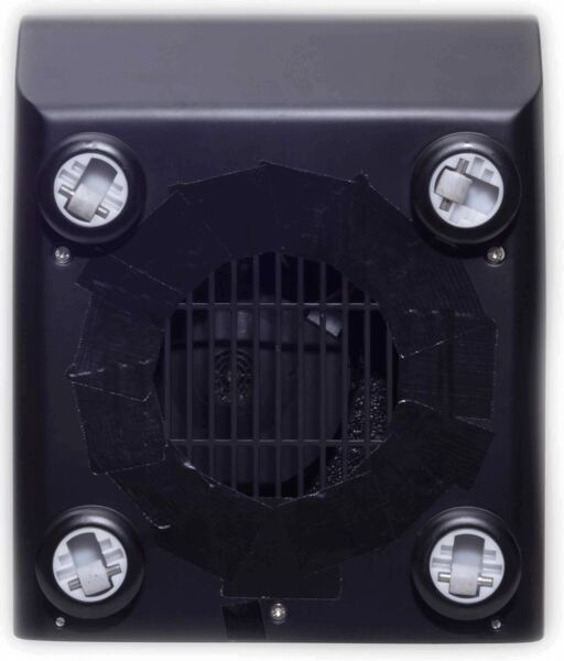 The image shows the back of a device. It has a square shape with a ventilation grid in the center, surrounded by a black ring. There are four round mounts at the corners.