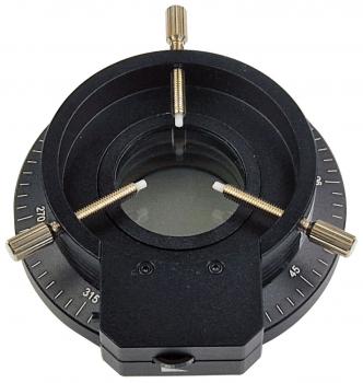 The image shows a black optical instrument with a circular opening in the center. Edges are marked with angle indicators. It has two small screws for adjustment.