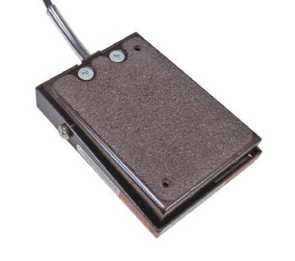 The image shows a rectangular, flat device with a rough surface texture. It has two push buttons on top and a cable that leads out from the side. The color is dark brown.