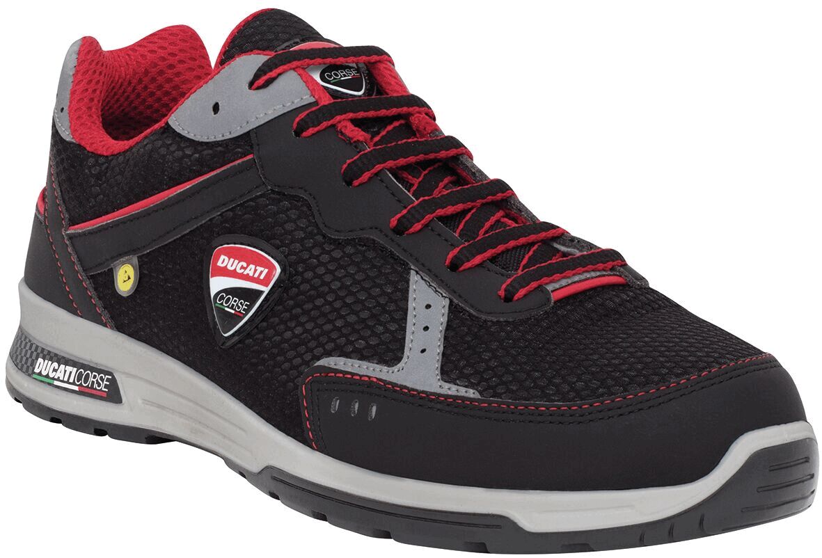 The shoe is sporty and predominantly black, with red accents. It has a breathable surface, gray details, and a sturdy, light sole. Logo visible on the side.