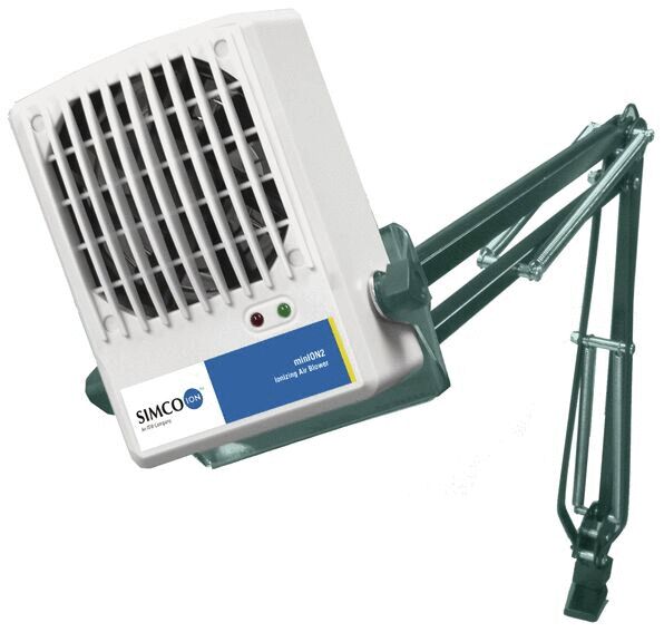 The image shows a white-gray fan attached to a movable arm. The arm is made of metal and is green. The fan has a grid for air circulation and a small control light.