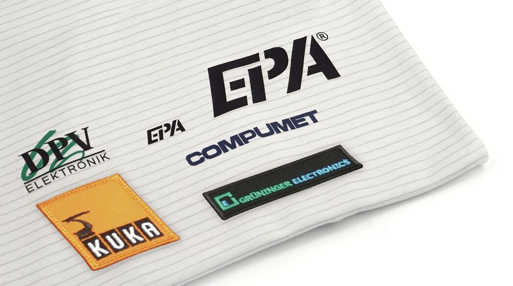 The image displays various logo patches on a light, striped fabric. The logos are from companies such as EPA, KUKA, and Computmet, among others. The predominant colors are black, blue, orange, and green.