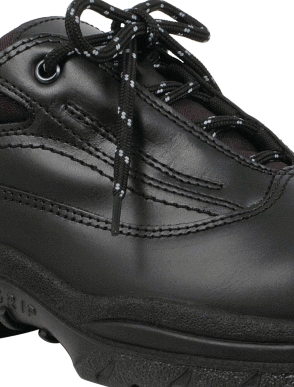 The image shows a black shoe with a flat sole and light-colored laces. The surface is smooth and has several seams that give it a sporty appearance.