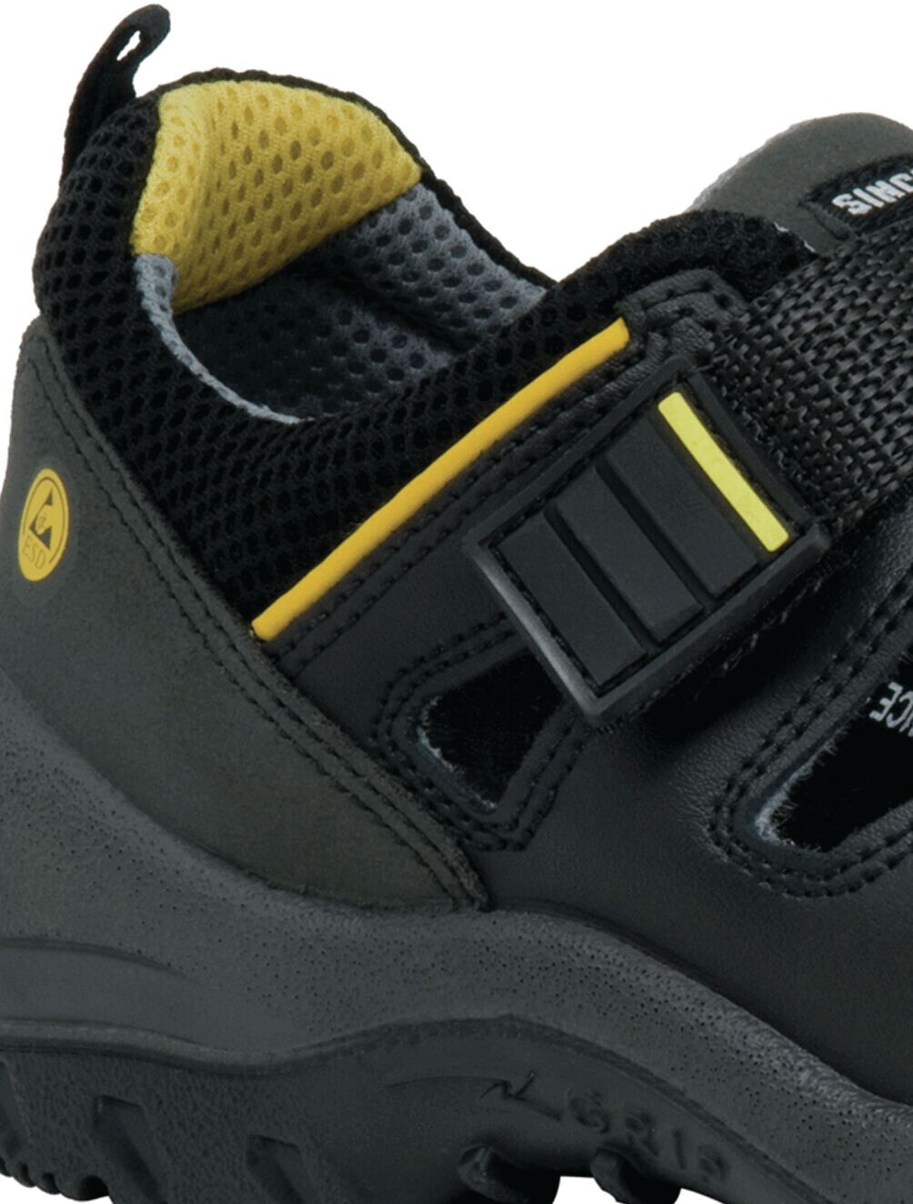 The image shows a black children's shoe with a breathable perforated pattern and a Velcro fastener. Yellow accents are visible on the top and the lining. The sole is sturdy.