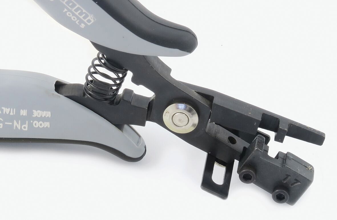 The image shows a pair of pliers with gray and black handles. It features a spring mechanism to open the pliers and a special device on the head for precise tasks.