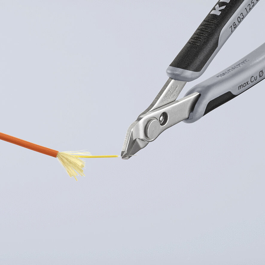 The image shows a pair of pliers gripping a fine, orange wire. The wire has a fan-shaped, yellow structure at the end. The background is neutral and bright.