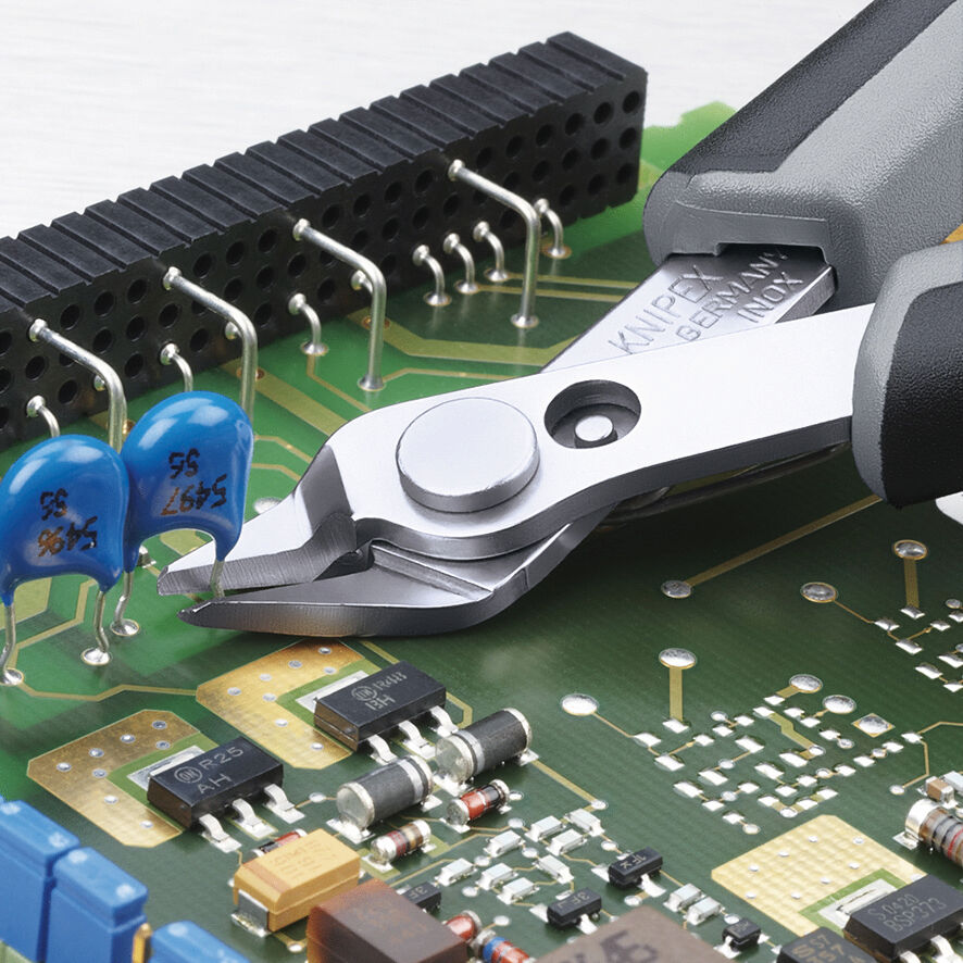 The image shows an electronic board with various components such as resistors and chips. A pair of pliers is grabbing a blue component on the board.