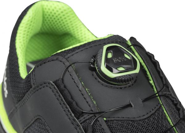 The image shows a black sports shoe with green accents. On the top, there is a quick-release system that allows for a convenient, lace-free adjustment.