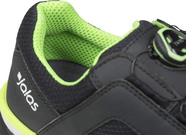 The image shows a black sports shoe with green accents. The interior is made of breathable mesh material, and the lacing system consists of a convenient snap closure.