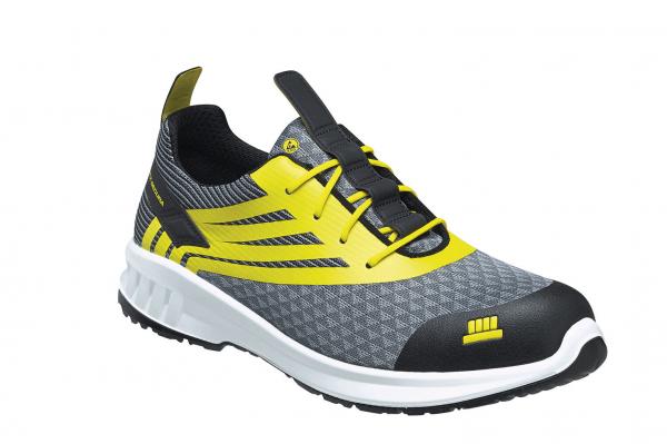 The shoe is a gray sneaker with yellow accents. It has a sporty design, a textured surface, and a black, reinforced toe cap. The laces are in the center.